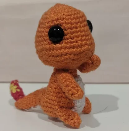 Side view of a Charmander crochet plushie, made from orange, red, yellow, and cream yarn.
