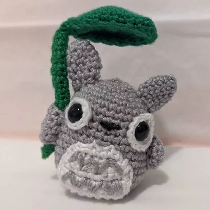 A crochet plushie of the character Totoro from the movie My Neighbour Totoro. The plushie is made of grey, dark green, and white yarn.