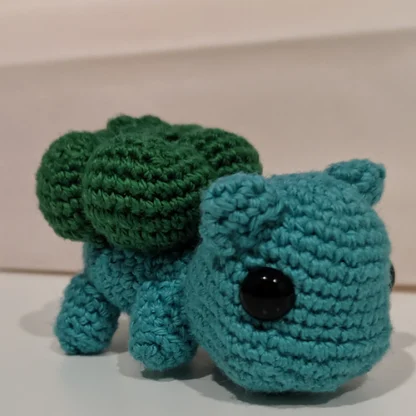 Side view of a Bulbasaur crochet plushie, made from teal, and dark green yarn.