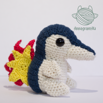 Side view of a Cyndaquil crochet plushie, made from dark blue, light yellow, red, and yellow yarn.