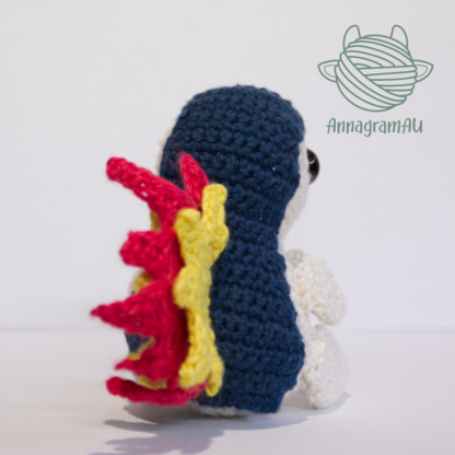 Back view of a Cyndaquil crochet plushie, made from dark blue, light yellow, red, and yellow yarn.